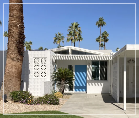 Casa blanca de arquitectura modernista, puerta azul, palmeras y cielo azul despejado