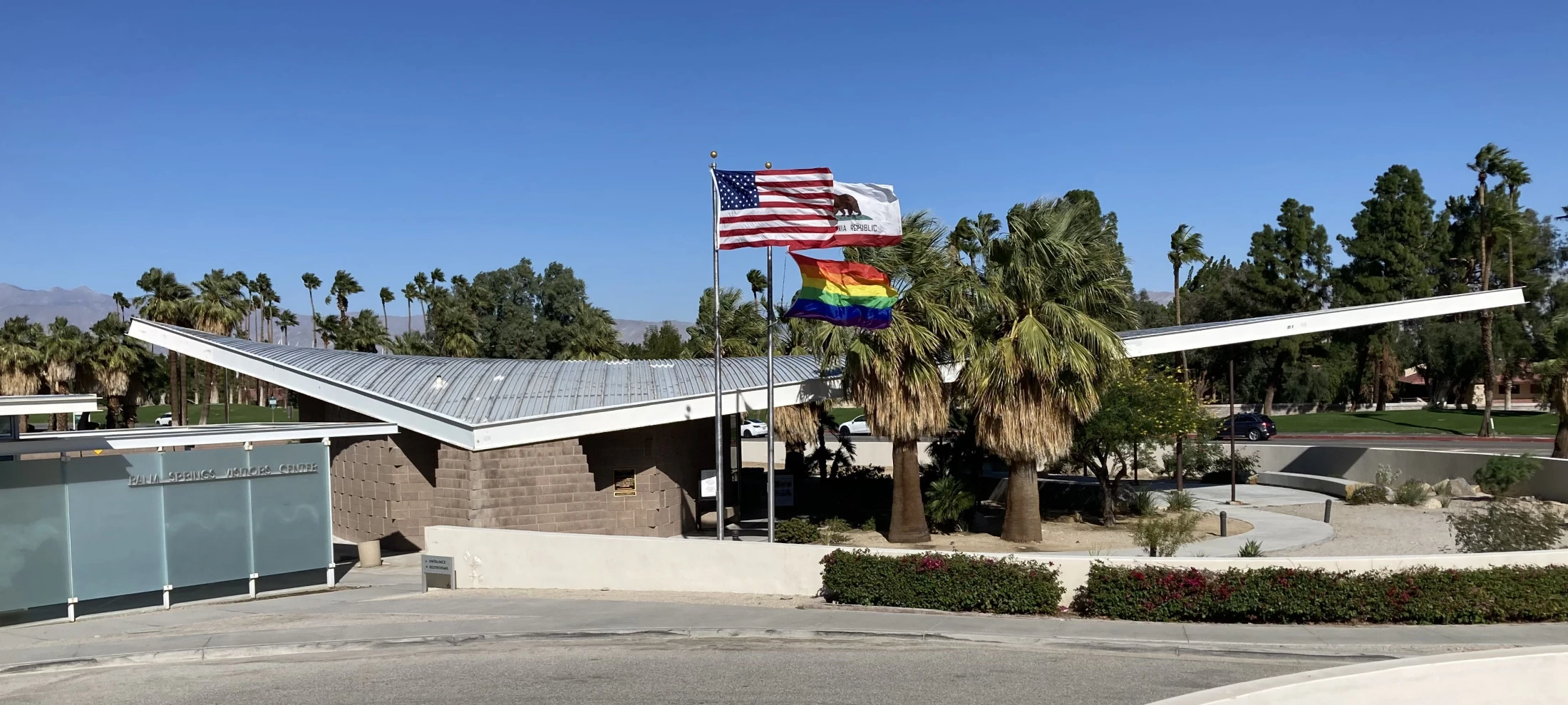 Wide view of the midcentury modern Palm Springs Visitors Center building with, American flag, California Republic flag, and LGBTQ+ flag