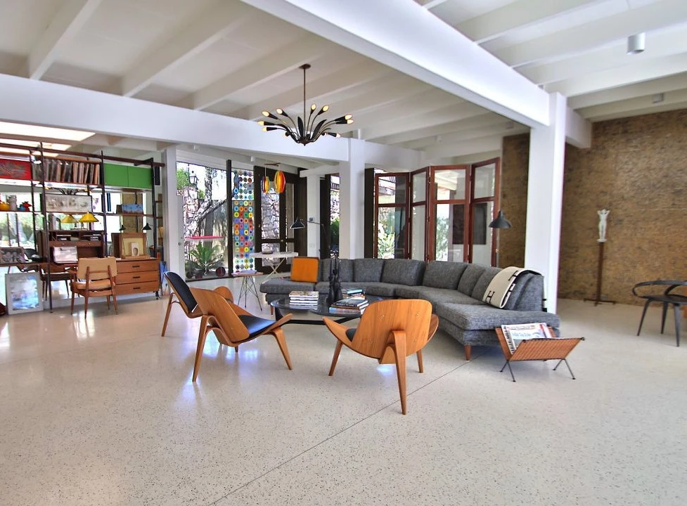 Interior of a midcentury modernist style home with a couch, table, and chairs with windows and glass doors in the background