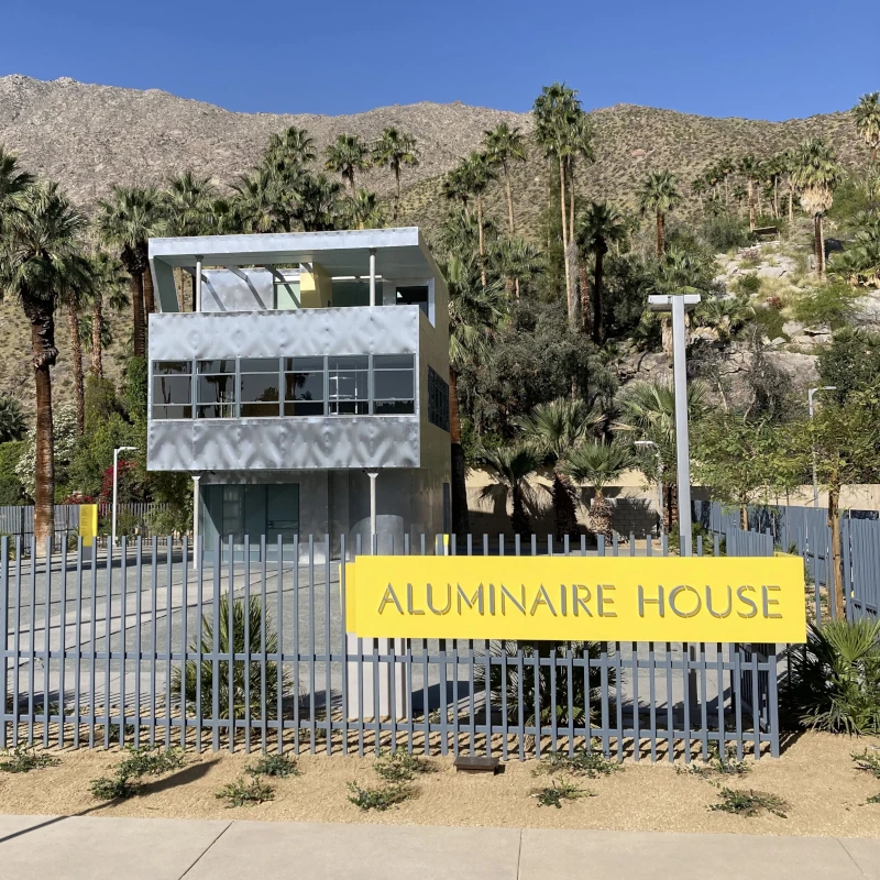 Front view of the Aluminaire House with lettered sign and Palm Springs desert landscape in the background